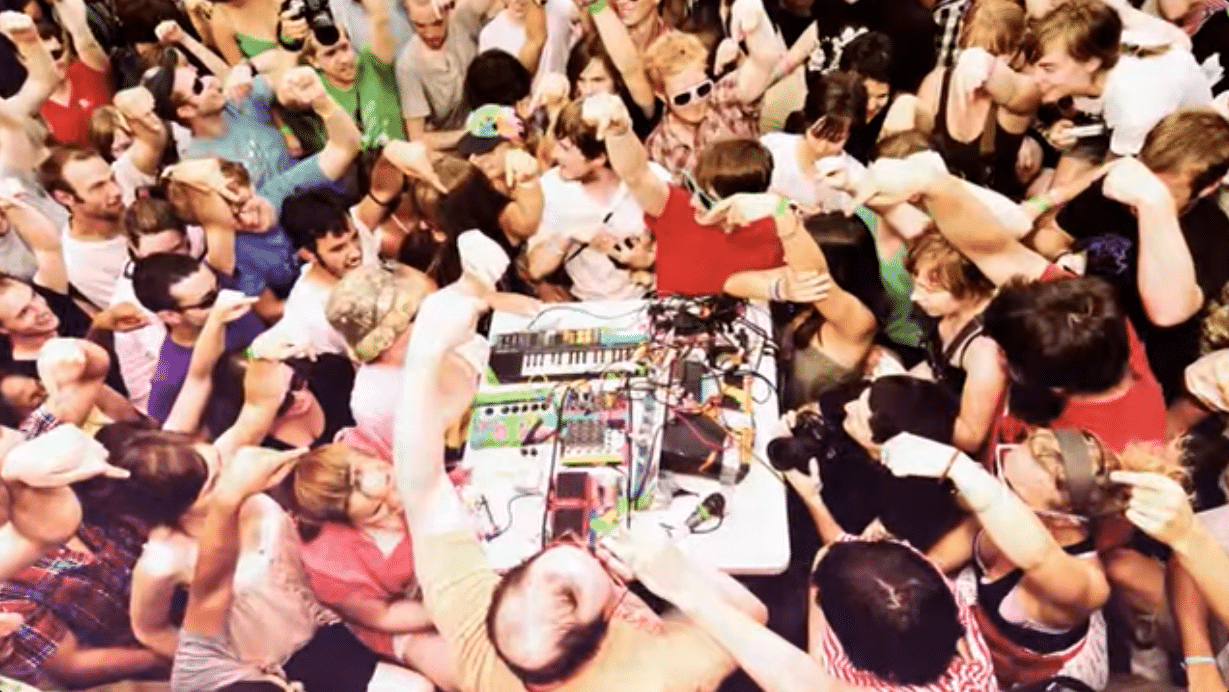 A still from WTMD's documentary "Do Whatever You Want, All the Time," showing a top down view of a crowd around a musician playing electronic music.