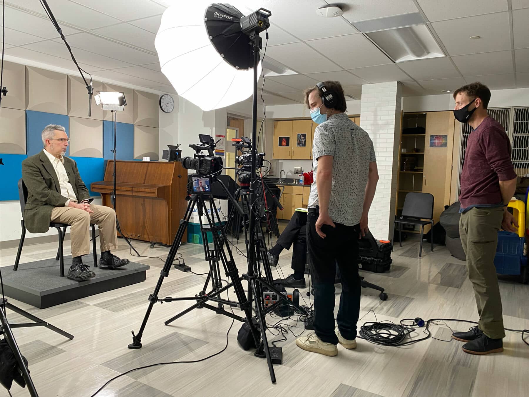 Matt and Kevin from Human Being Productions are providing production staffing services in the form of an interview. They are standing in front of cameras and lights, with a subject being interviewed in front of them.