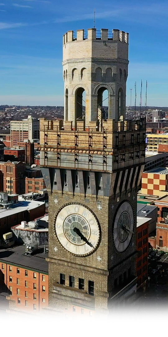 The Human Being Productions header image consists of a photograph of the Bromo Seltzer Tower in Baltimore Maryland. It is a brownish gray tower with a clockface, set against a clear blue sky. We are using this as an example of our video production and photography abilities.