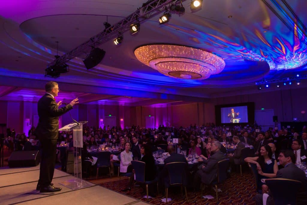 A man stands at a podium addressing a crowd at a special event.