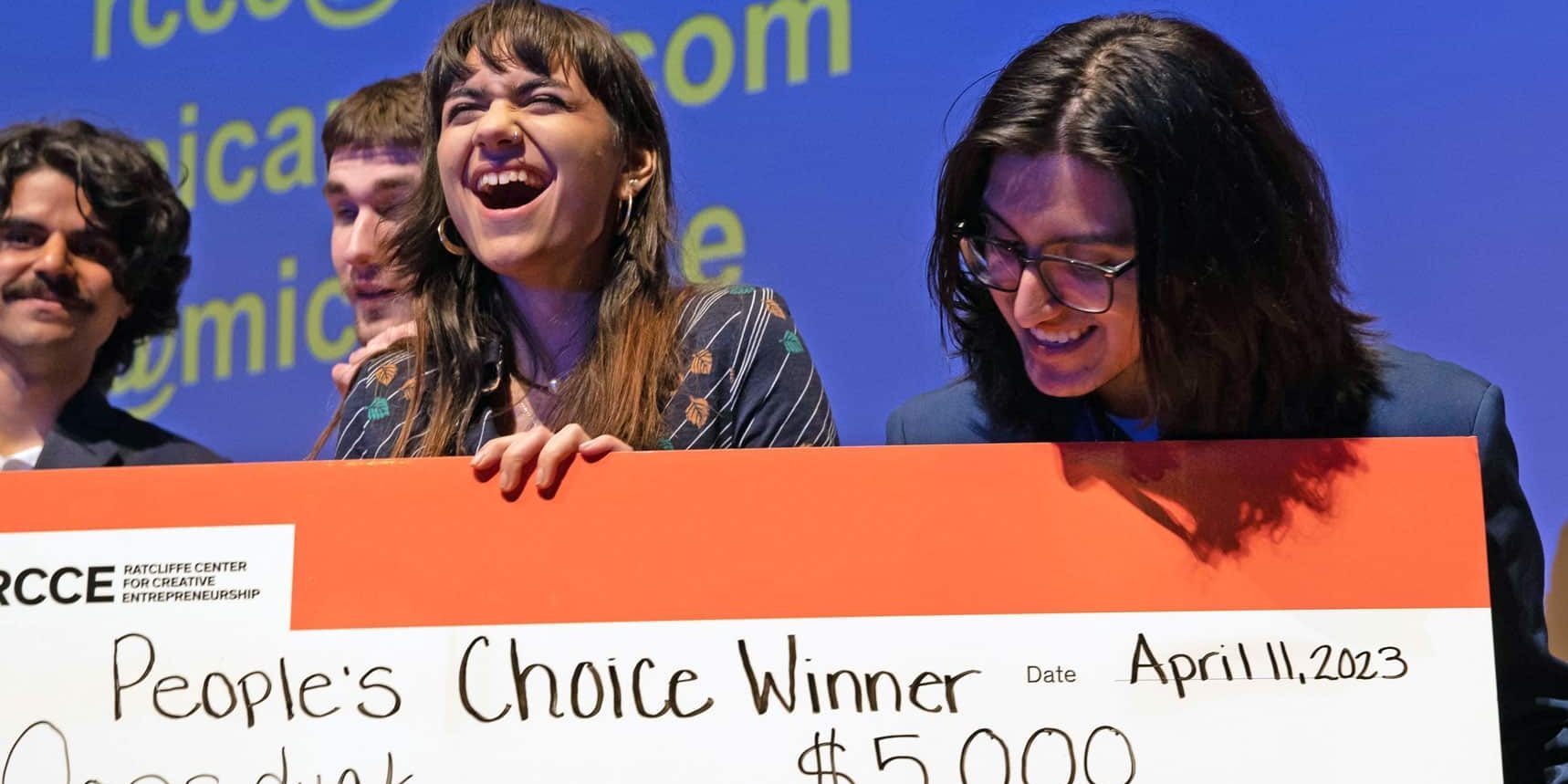Event Photography example: two students are holding a large check for $5,000 that they were just awarded on stage. They are smiling and looking incredibly happy.